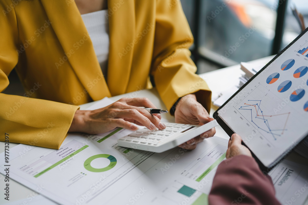 © amnaj - Two female entrepreneurs collaborate in the workplace, examining financial graphs and using a calculator to plan investment tactics © amnaj - Two female entrepreneurs collaborate in the workplace, examining financial graphs and using a calculator to plan investment tactics