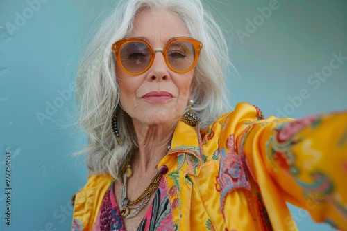 Stylish senior woman with grey hair and sunglasses taking selfie over blue background