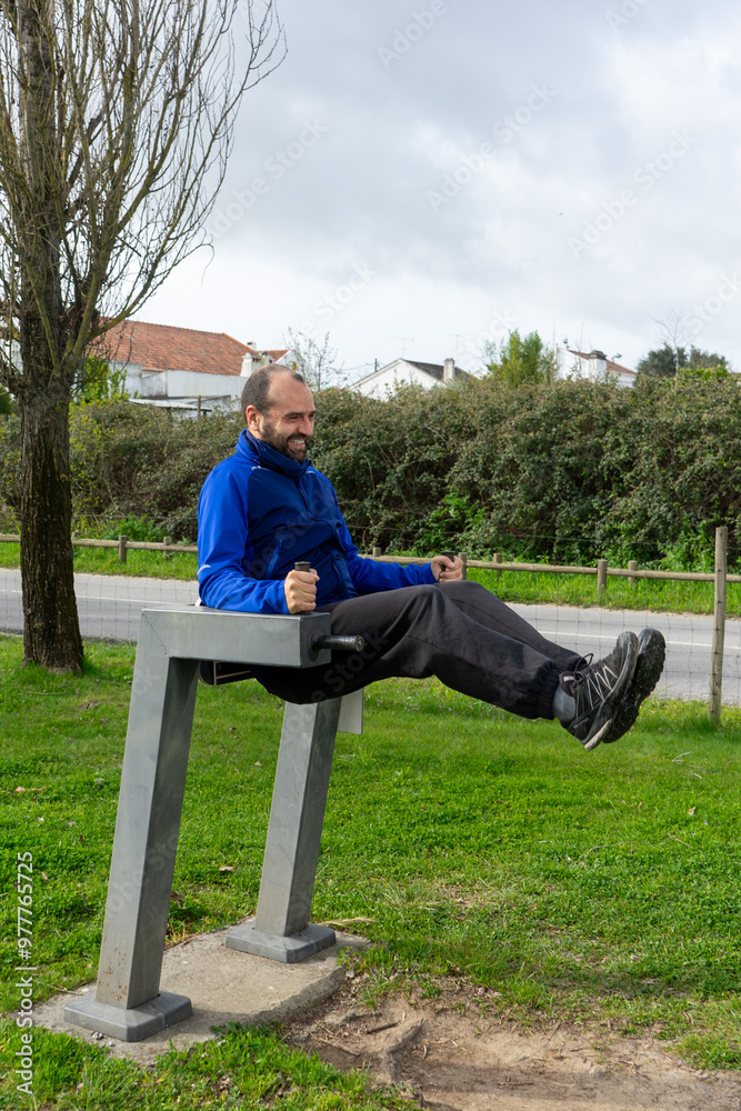Fototapeta premium Man doing sit-ups on an urban exercise machine in a public park, showcasing fitness and outdoor activity.