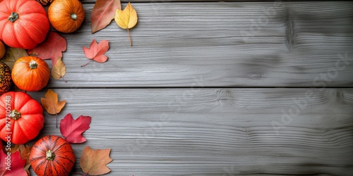 A minimalist autumn composition with pumpkins and colorful leaves scattered on a textured gray wooden background, creating a contrast between the vibrant foliage and muted wood