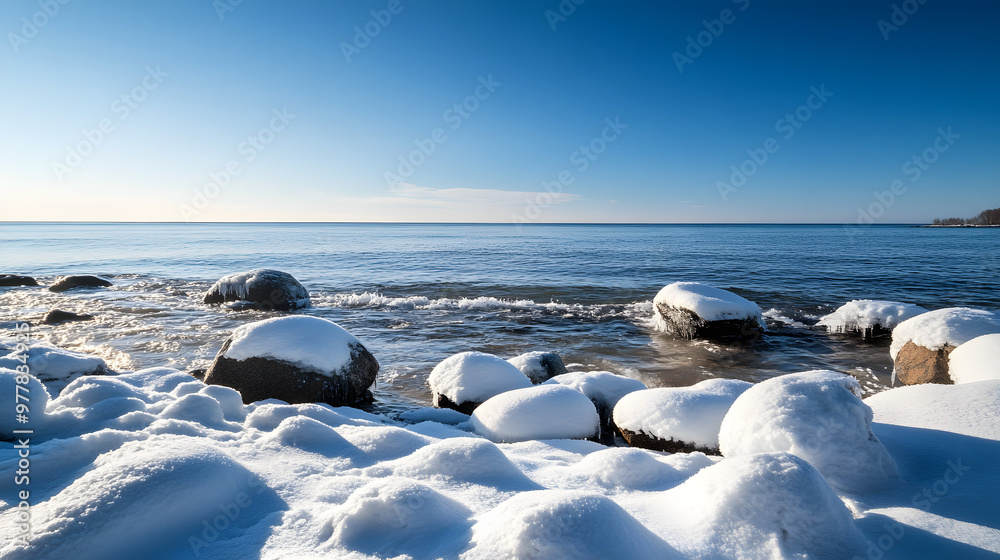 A peaceful winter morning by the sea with gentle waves lapping against snow-covered rocks and a clear blue sky above. A peaceful winter morning by the sea with gentle waves lapping against snow-covered rocks and a clear blue sky above.