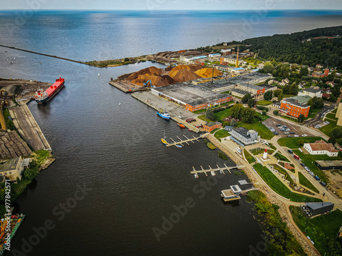 An aerial view of Salacgriva ship port, showcasing the marina with docks for small boats, a lighthouse, and surrounding greenery. The port area features well maintained pathways, parked vehicles photo