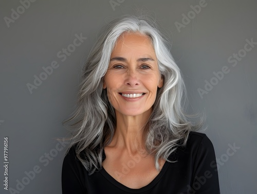 Radiant senior woman with silver hair smiling on a gray background