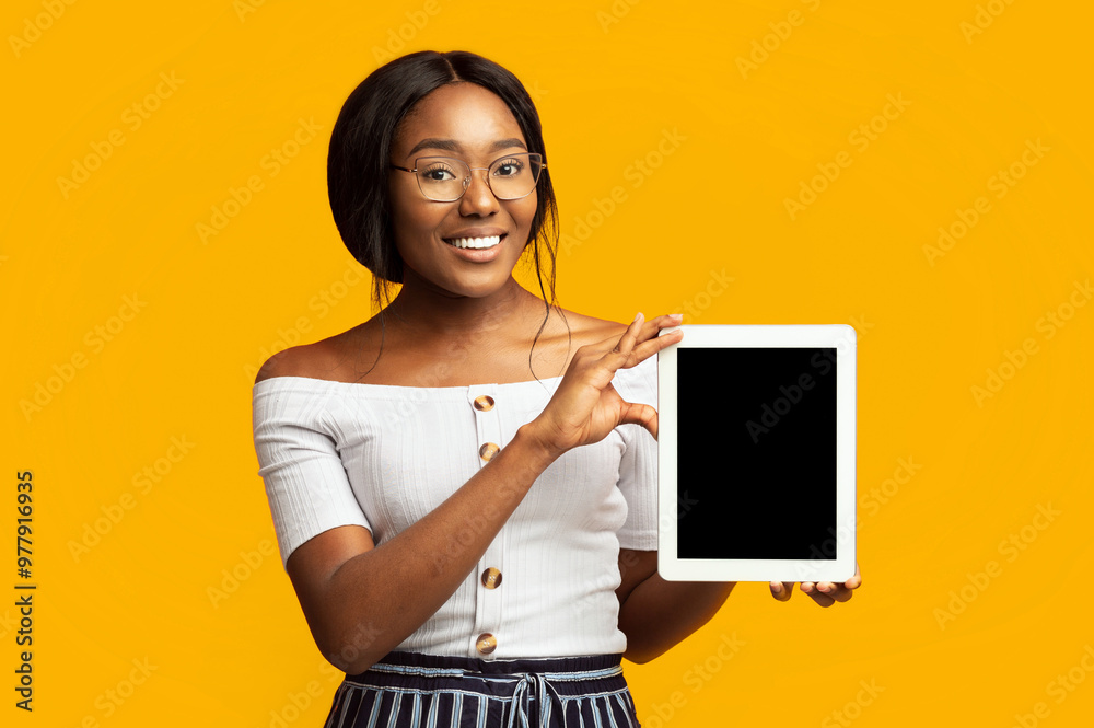 Afro Young Lady Showing Digital Tablet Empty Screen Smiling At Camera Standing On Orange Background In Studio. Mockup Afro Young Lady Showing Digital Tablet Empty Screen Smiling At Camera Standing On Orange Background In Studio. Mockup