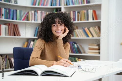 Cute young curly-haired woman sitting at the table in the library photo