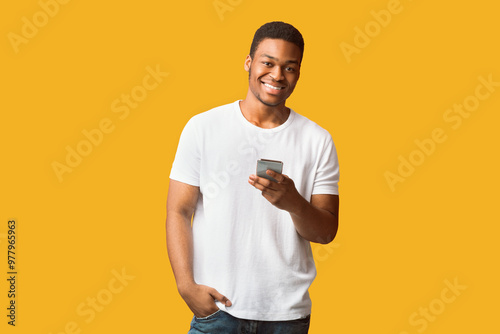 Money Transfer Online. Happy afro guy using mobile phone, looking at camera, copyspace, orange wall