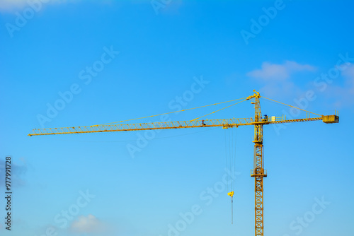 Construction yellow crane against the cloudy blue sky. Construction of houses, skyscrapers, and other buildings and housing. Free space and no one around.