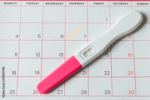 The pregnancy test with female ovulation day is on the calendar. Pregnancy test with two strips on calendar with marked date. The concept of expecting a baby, day of ovulation or conception of child. photo