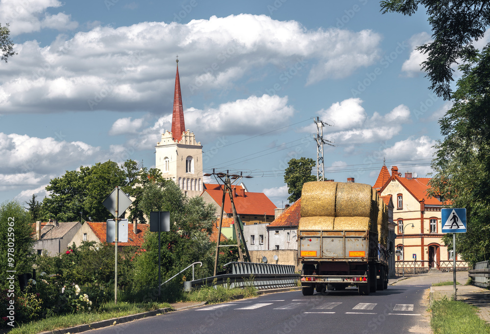 Summer cityscape of Nowe Miasteczko, Nowa Sól County, Lubusz (lubuskie). Agriculture: harvest season. Straw rolls in the trailer pulled by tractor.
