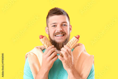 Portrait of happy young man with tasty hot dogs on yellow background