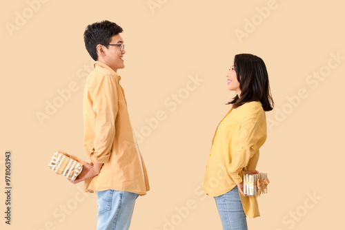 Young Asian friends greeting each other with gifts on beige background