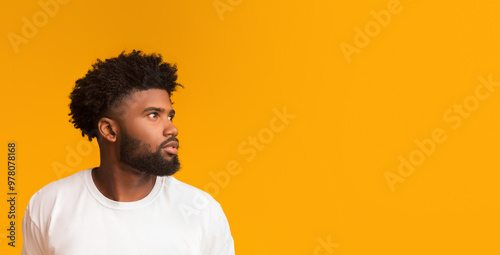 Skeptical young african american man looking aside at free space on orange background