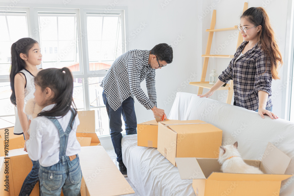 Asian family moving into new home. Parents and children packing and unpacking boxes in bright room with windows. Cat exploring cardboard box. Relocation, family bonding, and new beginnings concept. Asian family moving into new home. Parents and children packing and unpacking boxes in bright room with windows. Cat exploring cardboard box. Relocation, family bonding, and new beginnings concept.