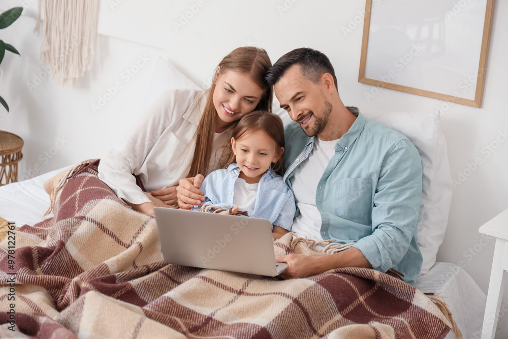 Little girl and her parents with warm plaid using laptop in bedroom Little girl and her parents with warm plaid using laptop in bedroom