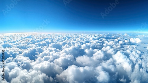 A panoramic view of fluffy white clouds floating across a bright blue sky, with the horizon barely visible.