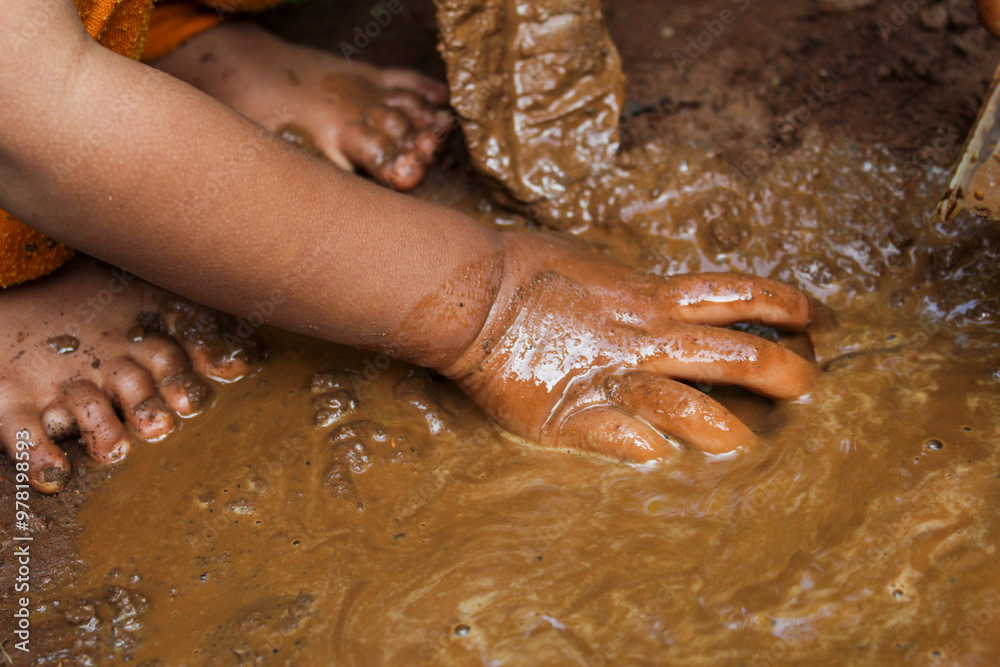 Fototapeta premium Little boy's hands are dirty with mud. Little boy playing with mud on the ground. Little children playing with mud