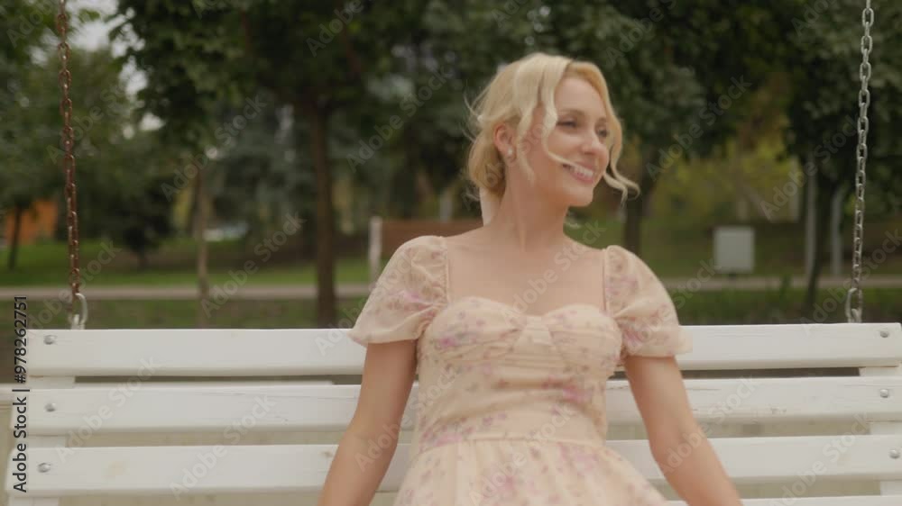Blonde Middle-Aged Woman Smiling on a Swing, Surrounded by Sunlight Blonde Middle-Aged Woman Smiling on a Swing, Surrounded by Sunlight