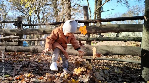 A small child tosses autumn leaves. Baby plays and throws up yellow leaves in an autumn park. Little boy is having fun on an autumn day, playing with fallen yellow leaves. Small child enjoys autumn