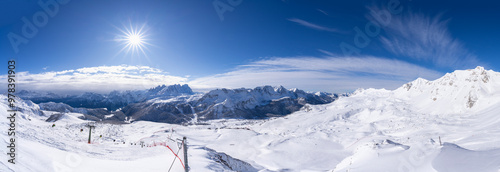 The image captures the icy splendor of San Pellegrinos snow-covered landscape bathed in sunlight, with ski lifts in the foreground and majestic mountain peaks in the distance.