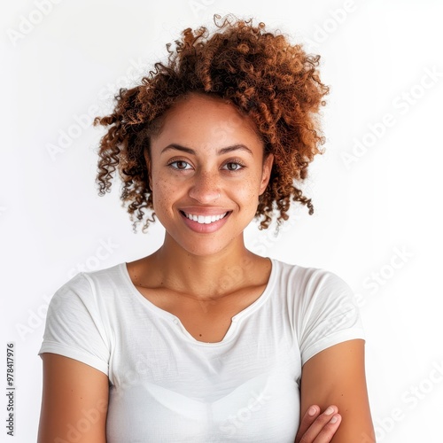 Confident and Radiant: A vibrant young woman with curly brown hair beams a genuine smile, radiating confidence and positivity. Her arms are crossed, showcasing a relaxed yet empowered stance. 