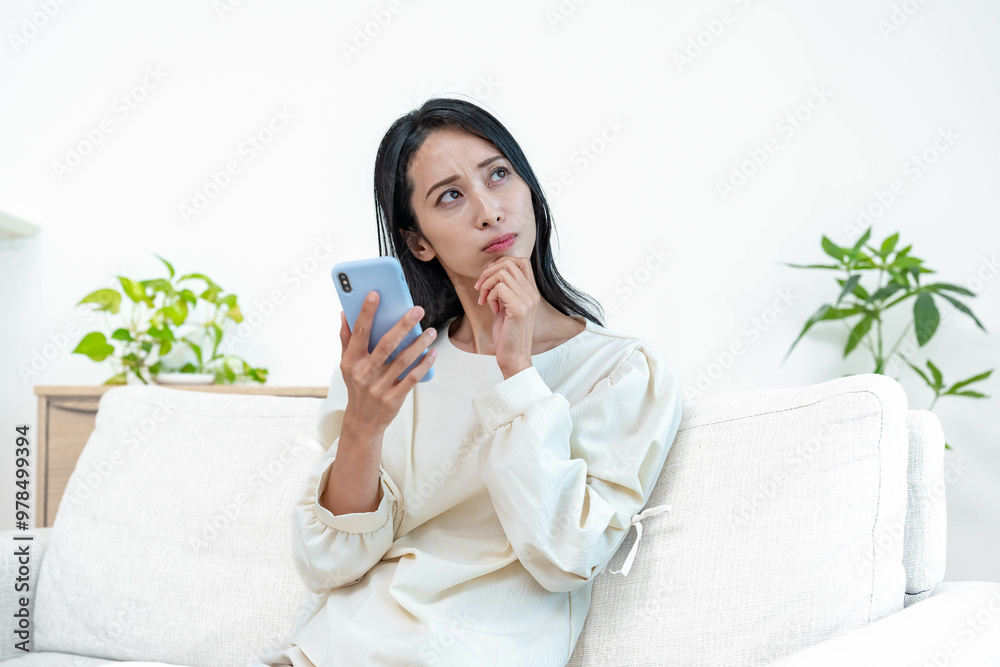 家のソファで携帯を持ち悩む女性