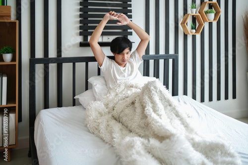 A young man adequate sleep,freshy waking up on bed,tranquil asian male sitting on bed and stretching arms in a bedroom at home photo