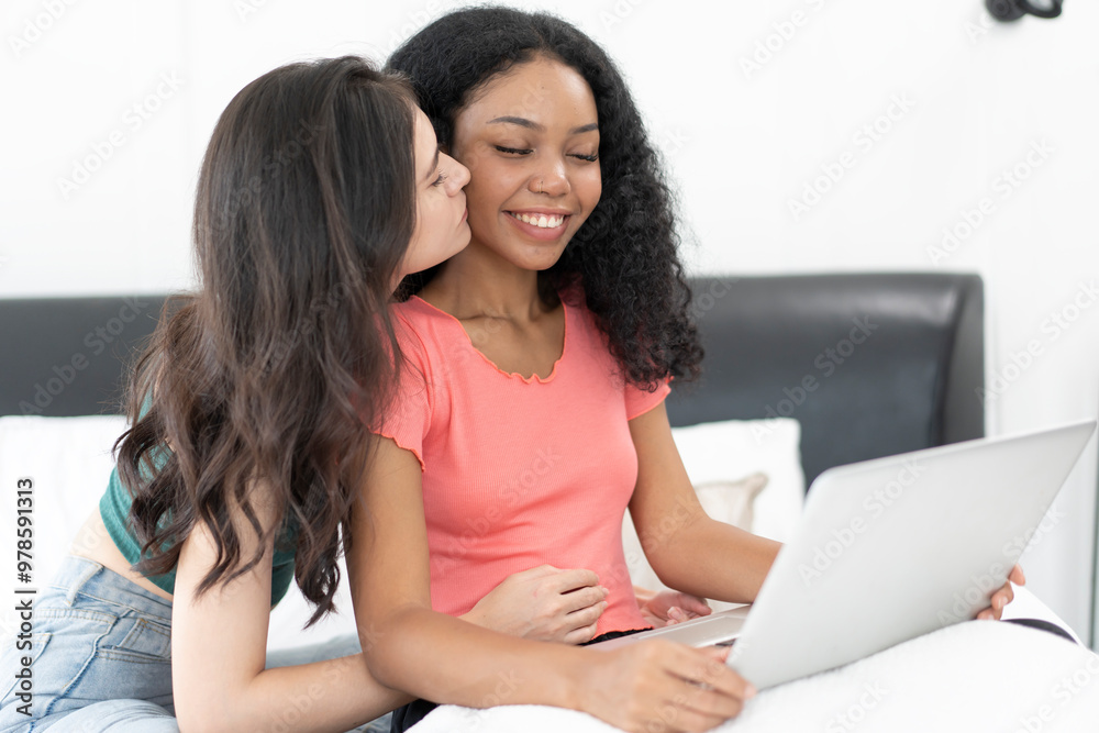 Happy lesbian couple using laptop on bed at home. Young multiethnic lesbian couple using laptop together in bedroom. Technology and love concept Happy lesbian couple using laptop on bed at home. Young multiethnic lesbian couple using laptop together in bedroom. Technology and love concept