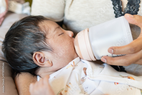 Mother is feeding her baby with formula milk in a bottle, very calm scene. the child is Caucasian and Latina with black hair and hair on her face.