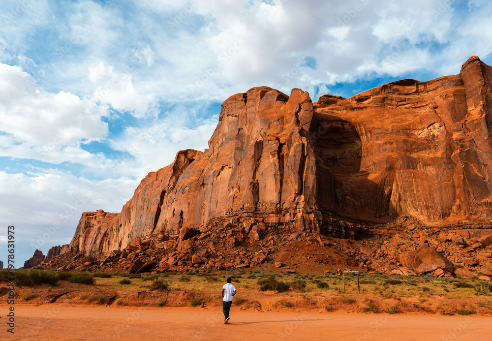 Man walking toward towering Rain God Mesa cliffs in Monument Valley Man walking toward towering Rain God Mesa cliffs in Monument Valley