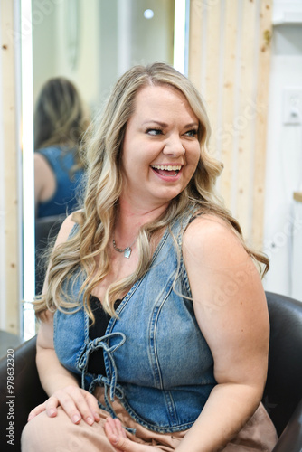 Blonde woman smiling, seated in a salon chair, wearing a denim v Free Download Blonde woman smiling, seated in a salon chair, wearing a denim v - GFXLoad