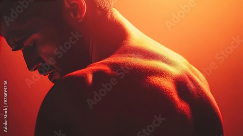 A dramatic close-up of a man's back illuminated by warm orange light, showcasing strength and emotion through shadows and contours.