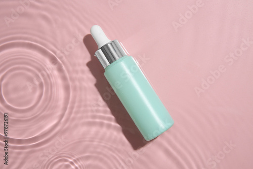 Bottle of cosmetic product in water on pink background, top view