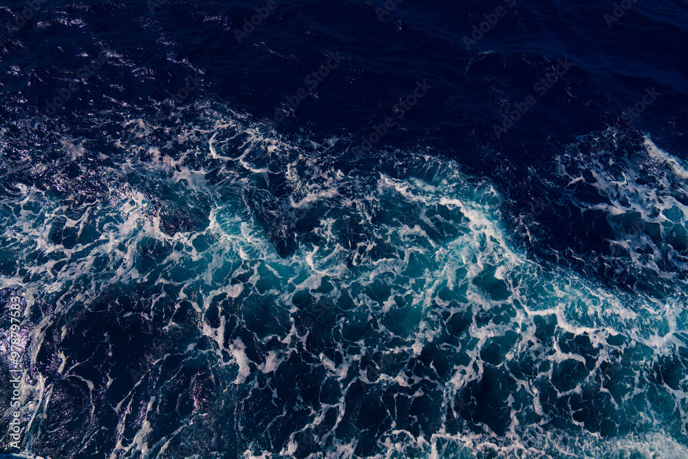 Fototapeta premium Aerial shot capturing the contrast between dark ocean waves and bright white seafoam, creating dynamic and dramatic seascape. Backgrounds or marine themes