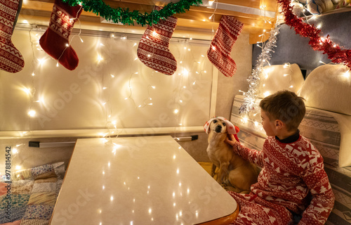 Boy dressed for Christmas with his dog wearing a Santa hat sitting inside a Christmas decorated motorhome