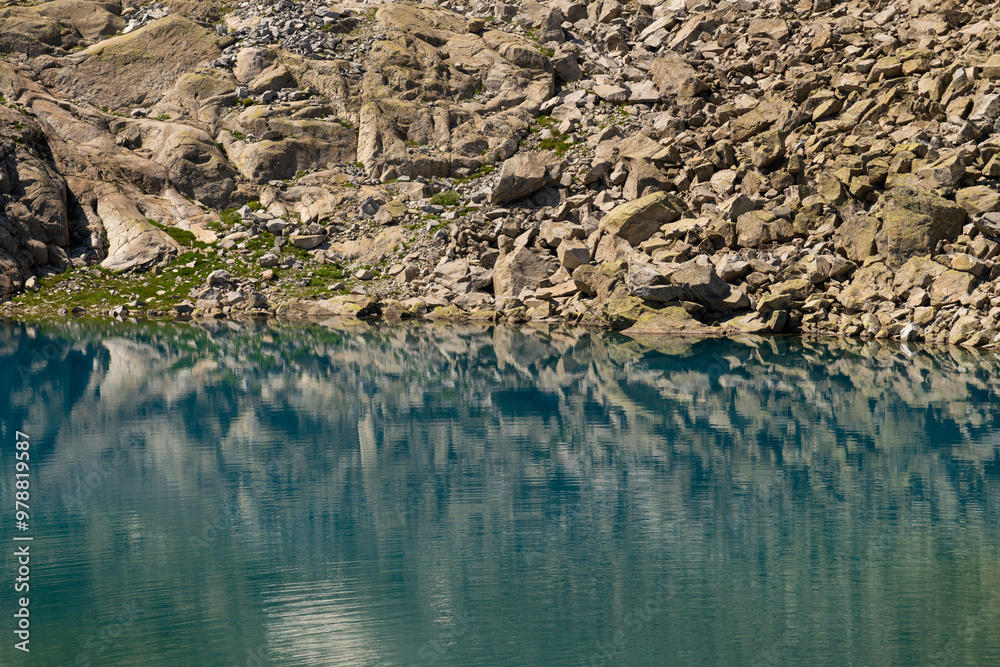 Obraz premium Serene mountain lake with crystal clear water reflecting rugged rocks and alpine scenery, showcasing untouched wilderness and natural beauty in a tranquil environment