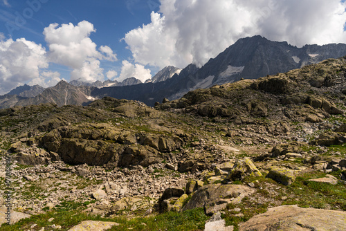 Dramatic view of rugged mountain landscape featuring rocky terrain and towering peaks, partially covered with snow. The scene is set under cloudy sky, raw and untamed beauty of the alpine wilderness