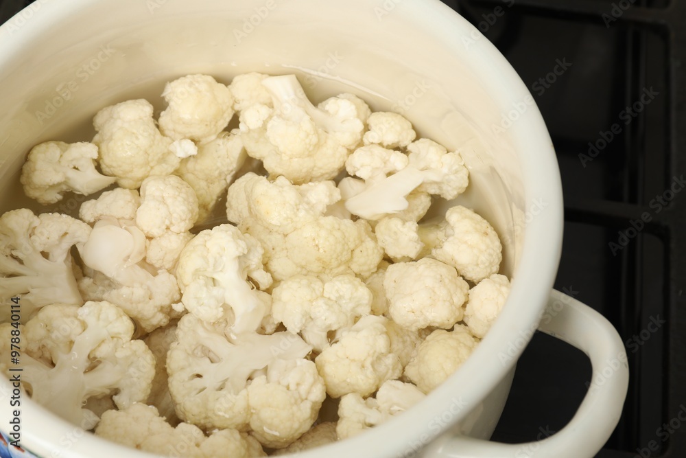 Cooking cauliflower. Florets in white pot with water on cooktop, closeup