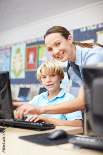 Woman, teacher and happy with boy on computer in classroom for help, teaching and learning. People, educator and smile on portrait with student at elementary school for education or brain development