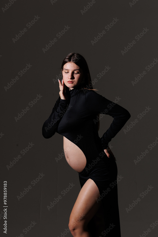 Beautiful young pregnant brunette girl. A woman waiting for a baby in a black dress, in the studio. Dress with a hole in the stomach, pretty pregnant belly. Beautiful young pregnant brunette girl. A woman waiting for a baby in a black dress, in the studio. Dress with a hole in the stomach, pretty pregnant belly.