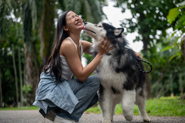 A woman is playing with her dog while taking it for a walk in a park. The dog licks her face.