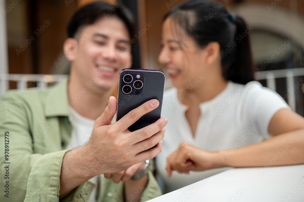 A man holding a phone to take a selfie with his girlfriend while they hang out together at a cafe. A man holding a phone to take a selfie with his girlfriend while they hang out together at a cafe.