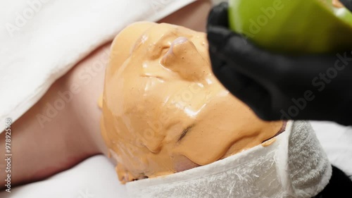 Close-up of a cosmetologist applying an alginate mask to a client's face with a spatula. The scene highlights professional facial skin care treatments in a beauty salon. photo