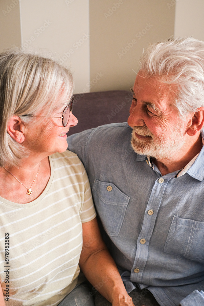 A vertical portrait of a mature couple sitting on the sofa at home, gazing at each other with love and affection. Capturing the essence of elderly lifestyle, first date romance, and relationship A vertical portrait of a mature couple sitting on the sofa at home, gazing at each other with love and affection. Capturing the essence of elderly lifestyle, first date romance, and relationship