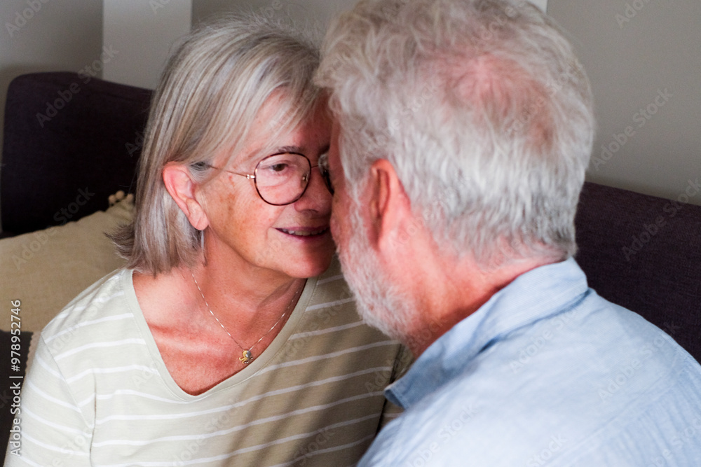 Heartwarming scene of a mature couple, a loving man and woman, cuddling on the sofa at home. The grandparents share sweet moments of affection, flirting and chatting leisurely indoors, enjoying Heartwarming scene of a mature couple, a loving man and woman, cuddling on the sofa at home. The grandparents share sweet moments of affection, flirting and chatting leisurely indoors, enjoying