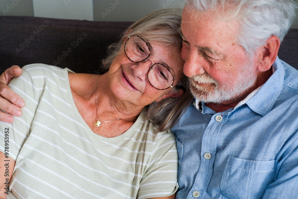 Close-up of an elderly couple embraced and happy on the sofa at home, both with dreamy and relaxed expressions. They enjoy their long-lasting love and friendship, showcasing mature, healthy Close-up of an elderly couple embraced and happy on the sofa at home, both with dreamy and relaxed expressions. They enjoy their long-lasting love and friendship, showcasing mature, healthy