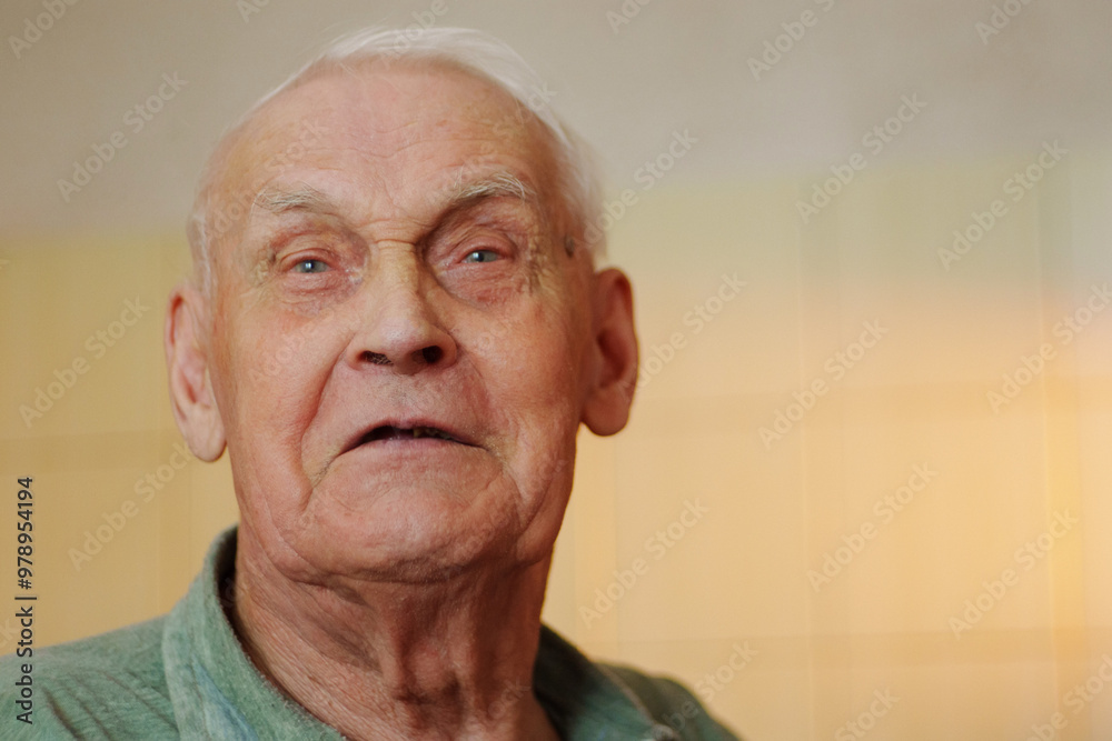 Obraz premium An elderly man is portrayed with a thoughtful expression, sitting indoors. The soft lighting emphasizes his features, reflecting a lifetime of experiences.