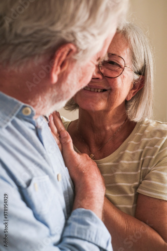 Portrait of a mature couple embracing each other in their home, posing affectionately for a photo in front of the camera. They share a loving glance after a lifetime together, smiling in casual