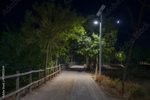 A solar-powered streetlight stands tall at night along a tranquil park path, the solar panels are installed on top of the streetlight, absorbing sunlight and converting it into electricity, Spain photo