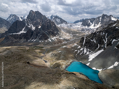 Aerial view of majestic snow-capped mountains and a serene lake surrounded by rugged terrain, Deosai National Park, Gilgit-Baltistan, Pakistan.