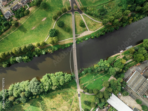 Aerial view of serene river winding through lush green park with bridge and trees, York, England.
